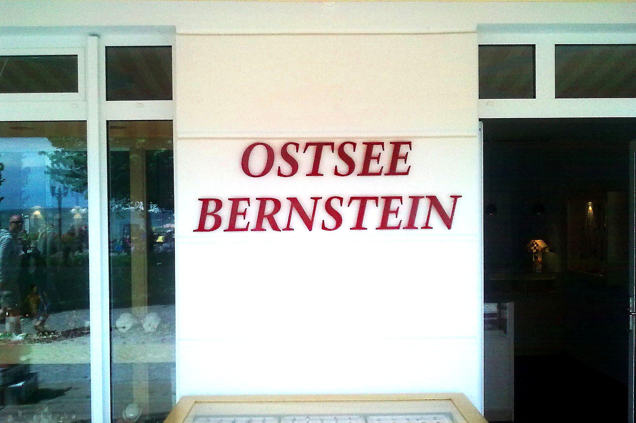 Schriftzug Ostsee Bernstein aus roten Einzelbuchstaben, plastisch auf die weisse Fassade zwischen Schaufenster und Eingang gesetzt