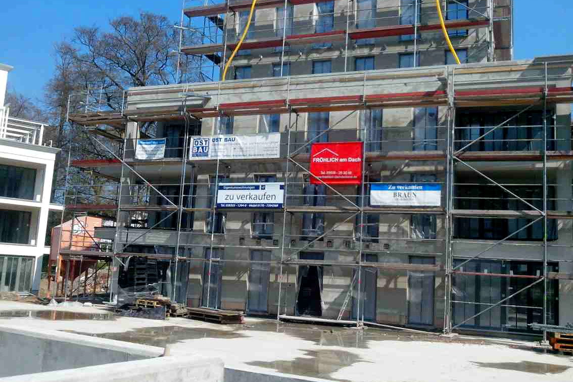 Mehrere gespannte Werbebanner nebeneinander am Baugeruest eines Rohbaus vor blauem Himmel
