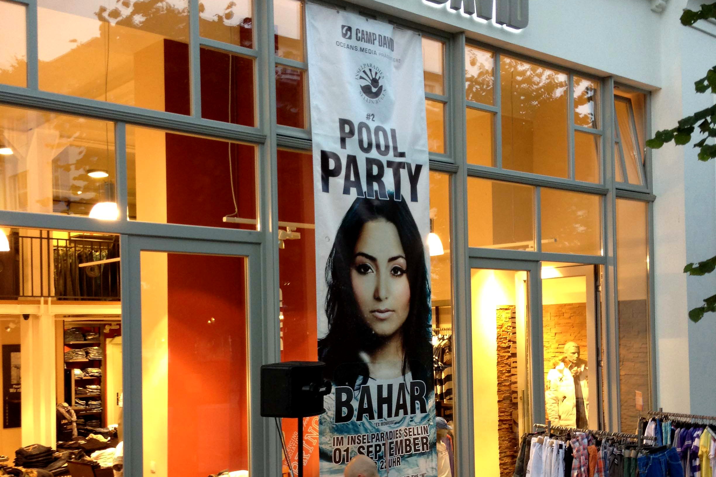 Hochformatiges Veranstaltungsbanner im Digitaldruck, abgehaengt vor der beleuchteten Schaufensterfront in Sellin