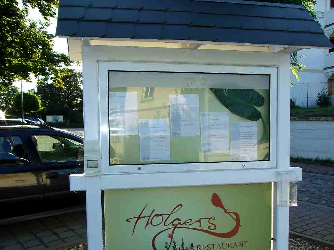 Freistehender Schaukasten des Restaurants Holgers mit Schindeldach, verglaster Aushangflaeche und beschrifteter Tafel